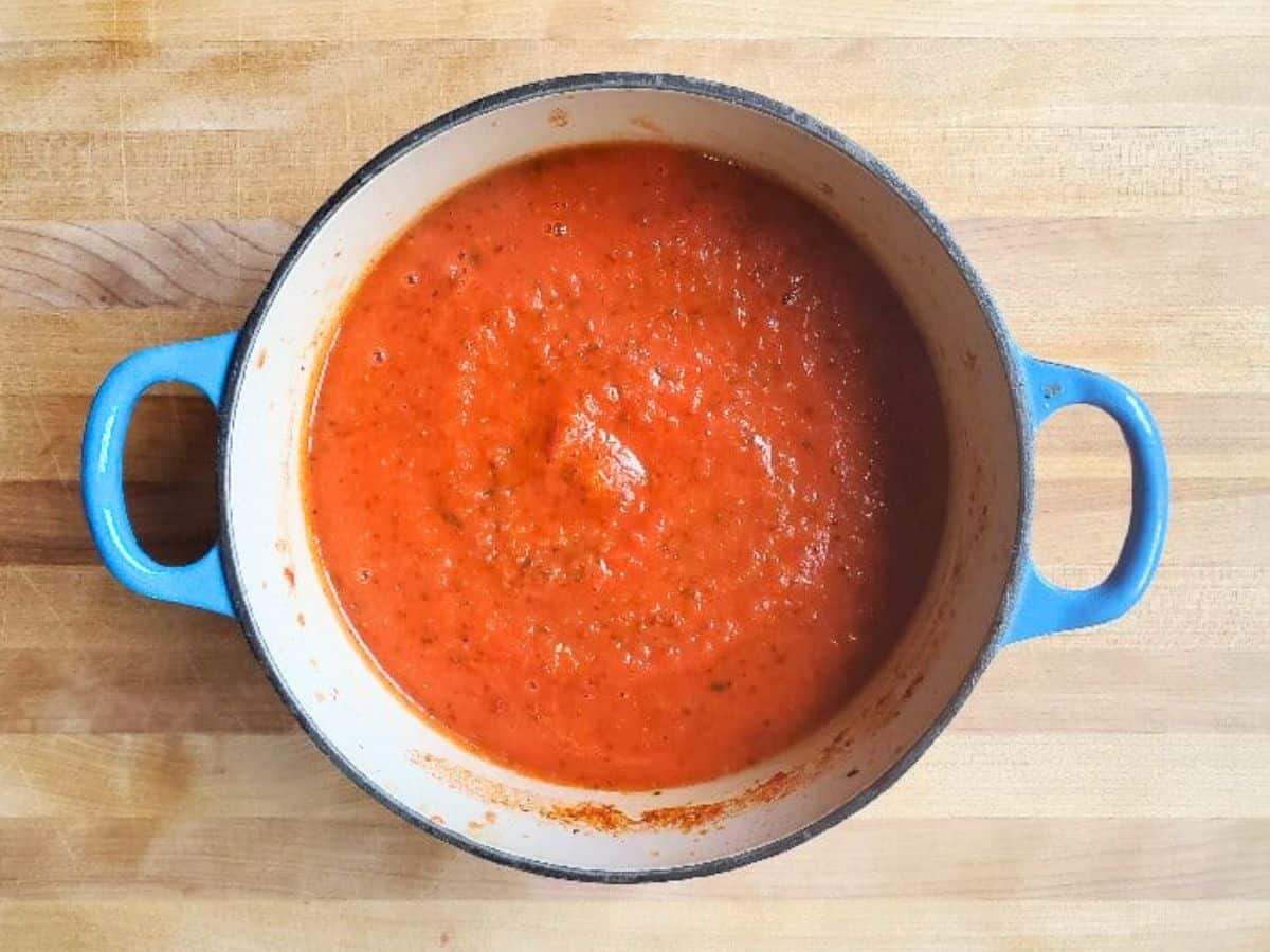 Image shows an overhead shot of a blue enameled cast iron pot with freshly made Marinara Sauce.