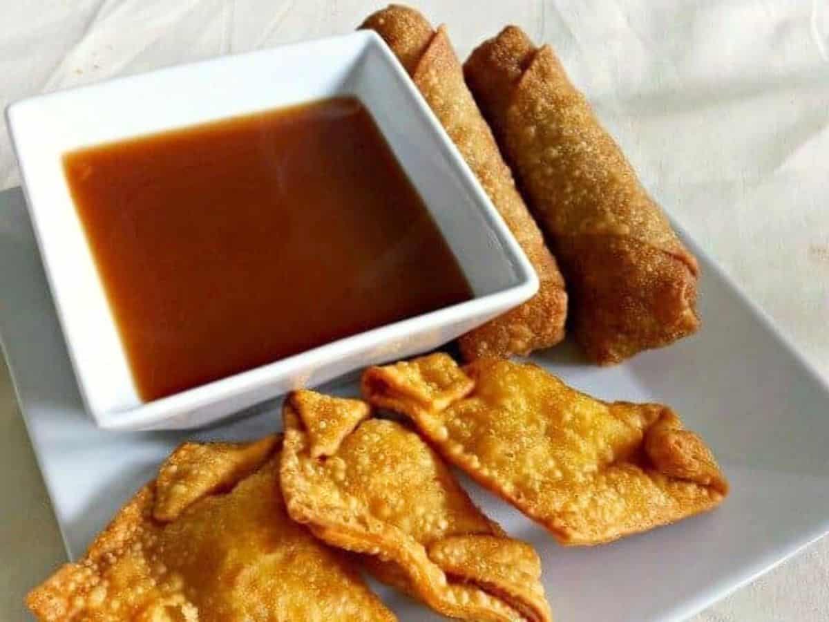Image shows an Egg roll dipping into homemade sweet and sour sauce in a white bowl.
