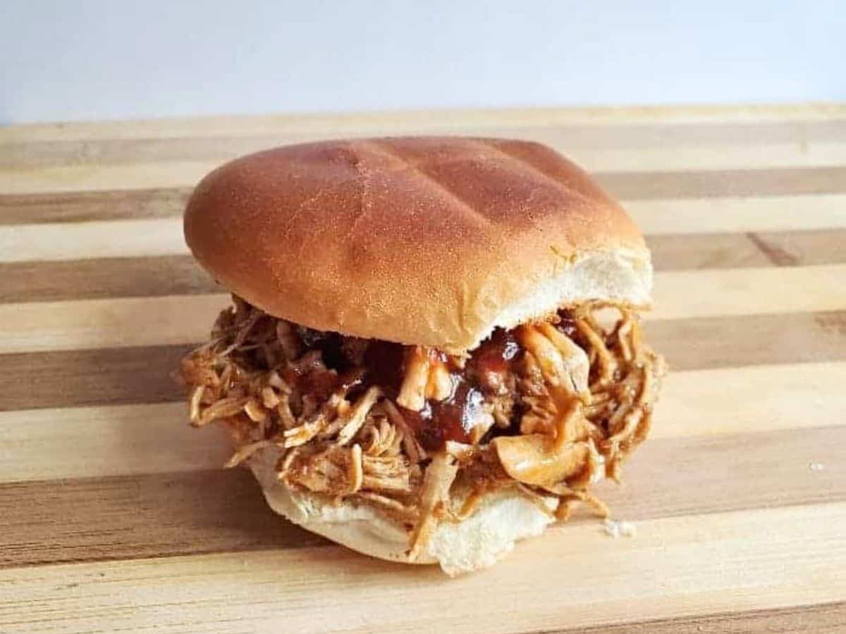 Image shows a BBQ shredded chicken sandwich on a wooden board.