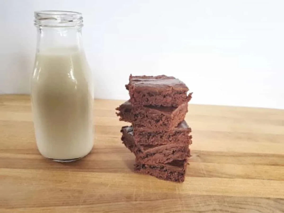 Texas sheetcake brownies stacked on a wooden board sitting next to a small jug of milk.