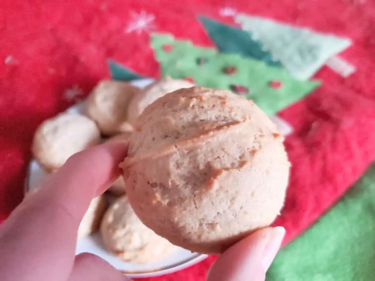 Image shows a hand holding an Egg Nog Cookie over a plate of more cookies.