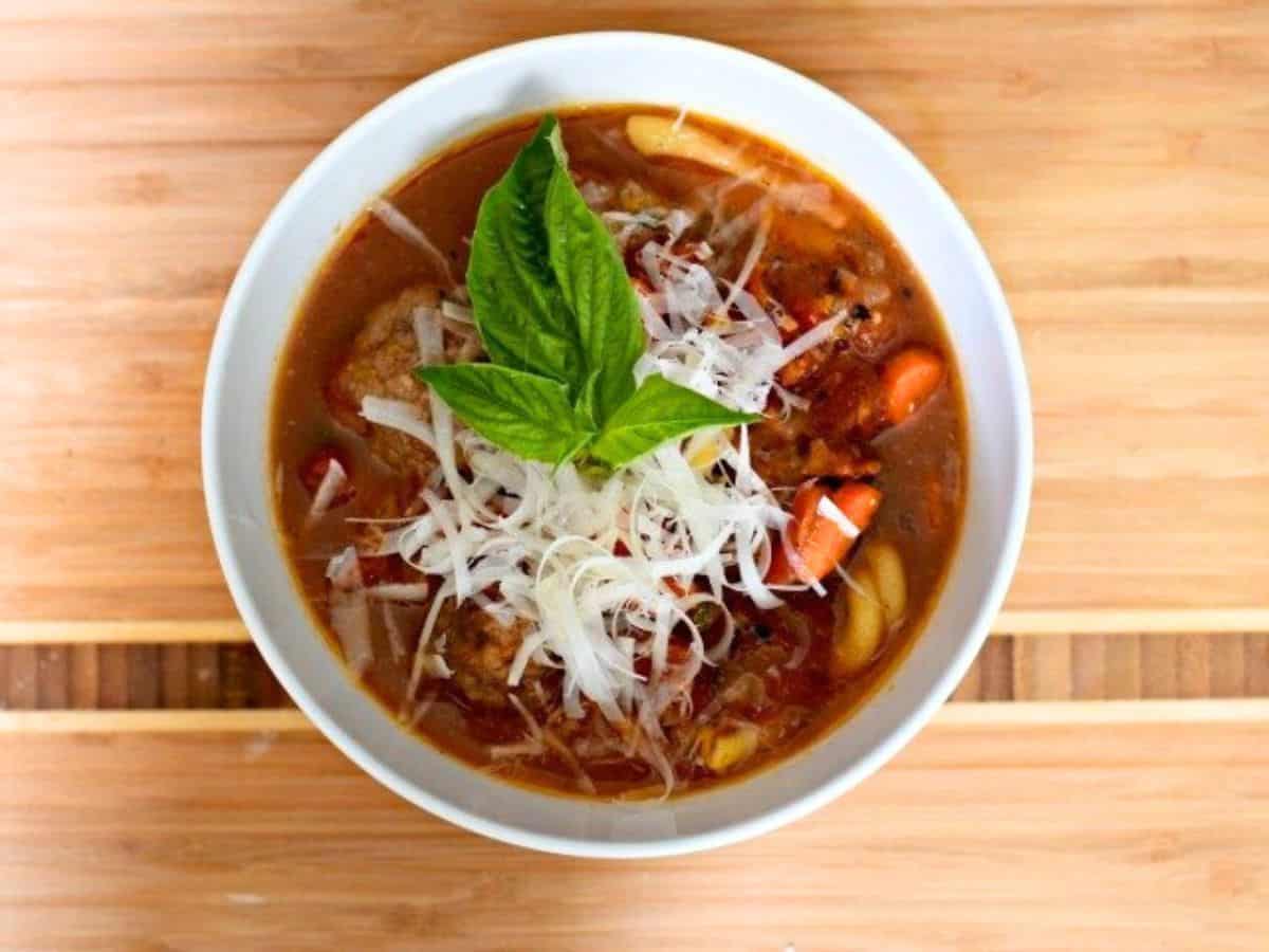 Image shows A bowl of italian meatball soup with a basil leaf on top.