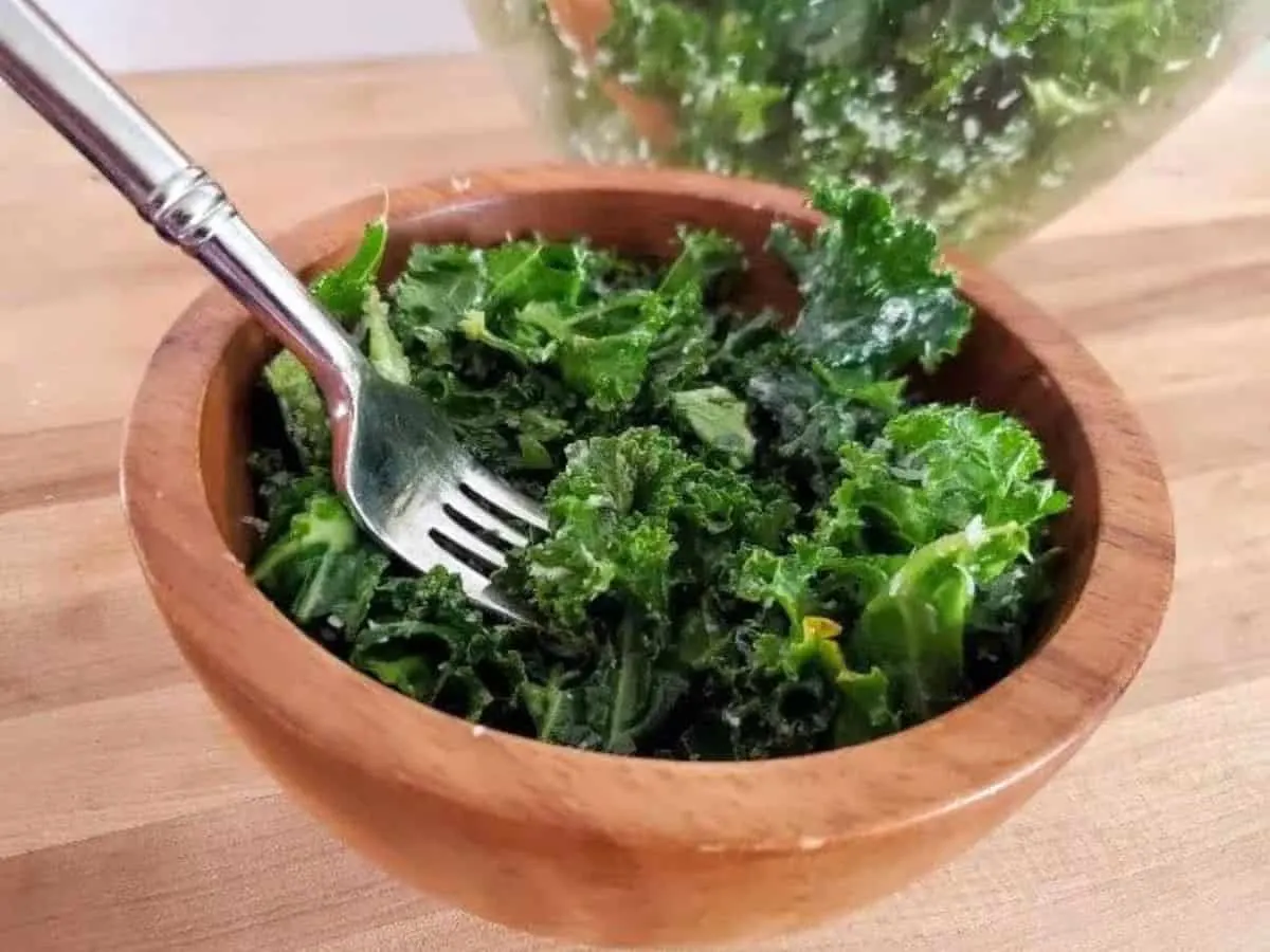 Image shows a fork holding a bite of lemon kale salad with the full bowl behind it.