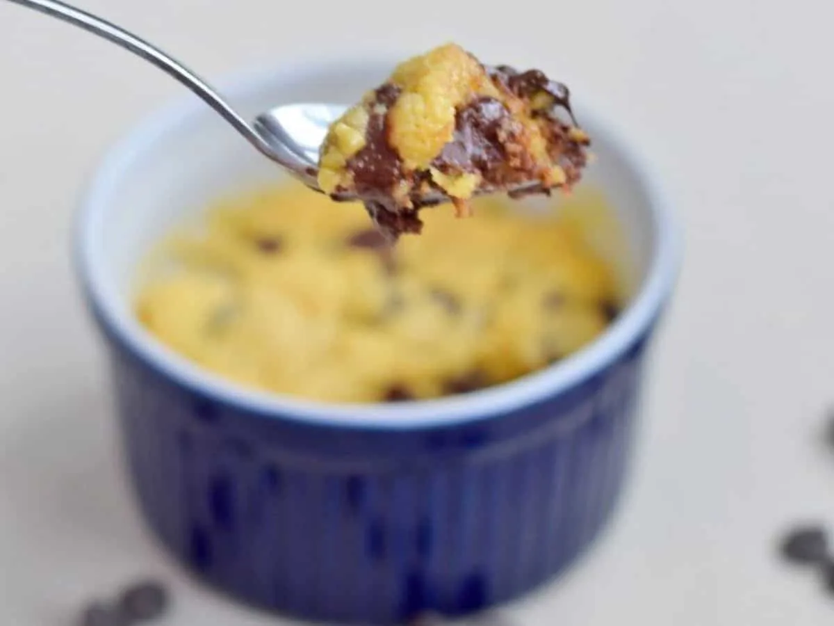 Image shows a close up of a spoon holding a bite of an Individual Chocolate Chip Cookie with the full cookie in the ramekin behind it.