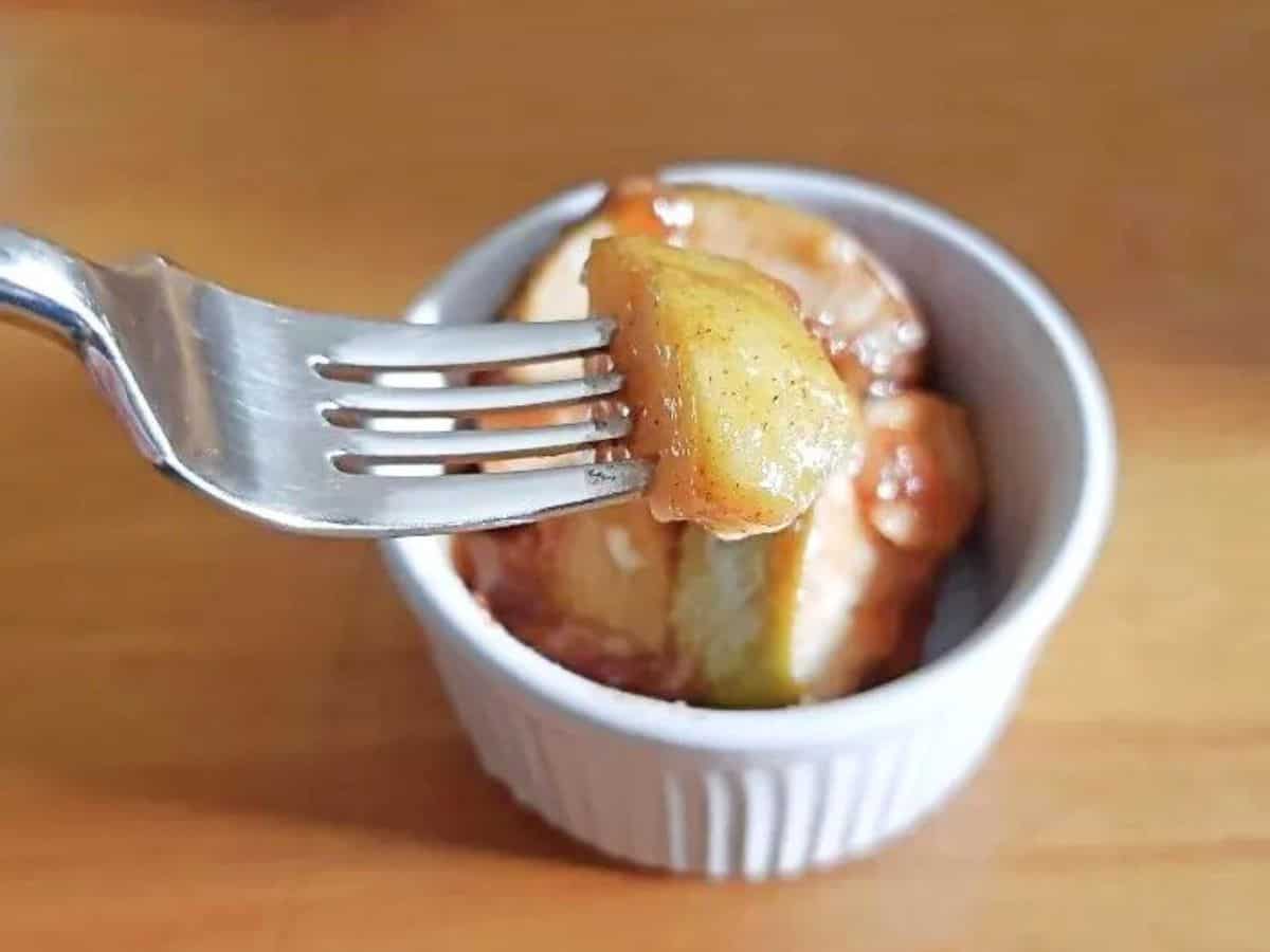 Image shows a Fork holding a bite of cinnamon apples with a ramekin holding more in the background.