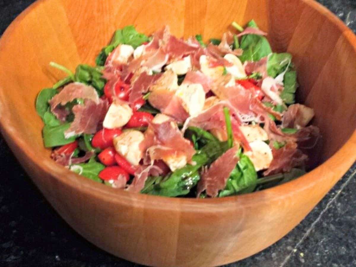 Image shows a Spinach Caprese Salad in a wooden salad bowl.