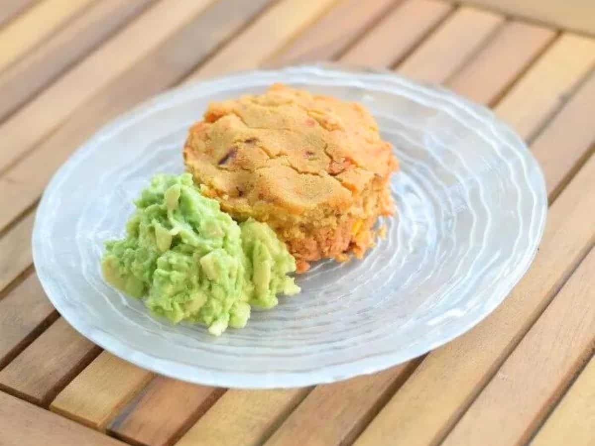 Image shows a Tamale pot pie on a glass plate with guacamole sitting next to it.