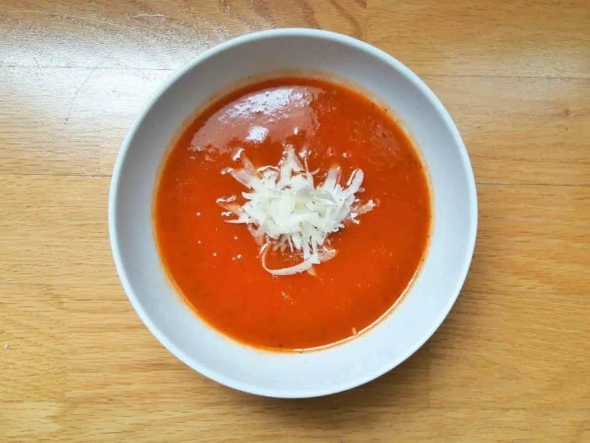 Overhead image of a bowl of tomato soup with parmesan grated into it.