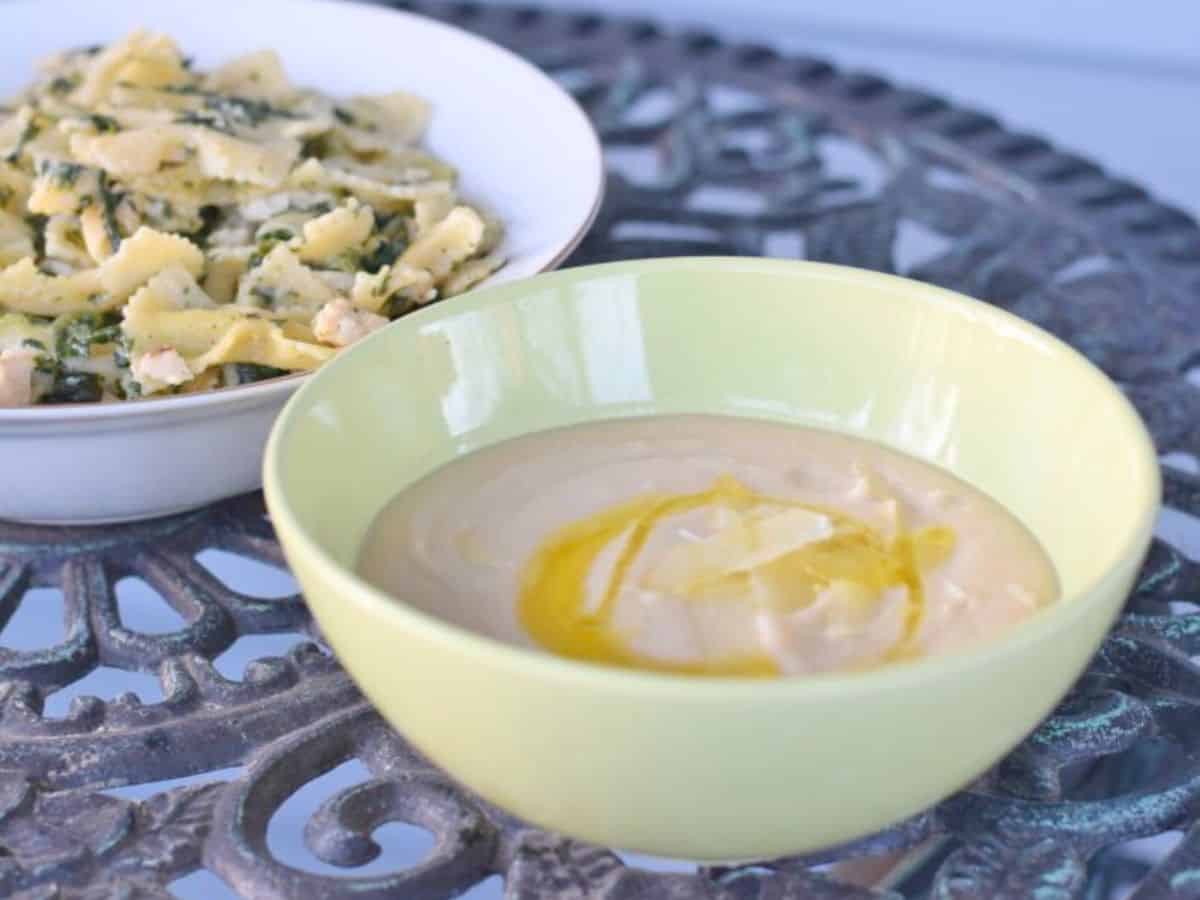 Image shows a bowl of Creamy Tuscan Bean Soup with a drizzle of olive oil in a green bowl.