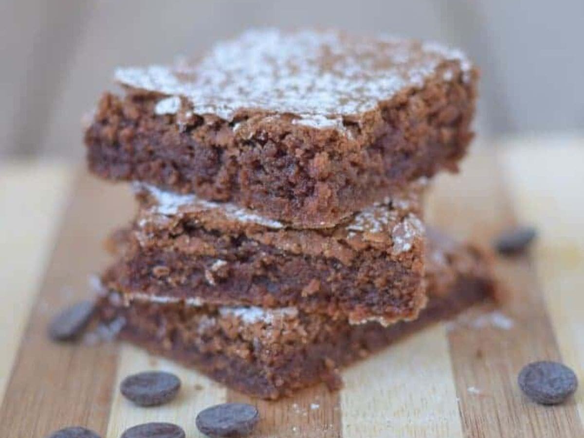 Image shows a stack of Classic Brownies on a wooden table.