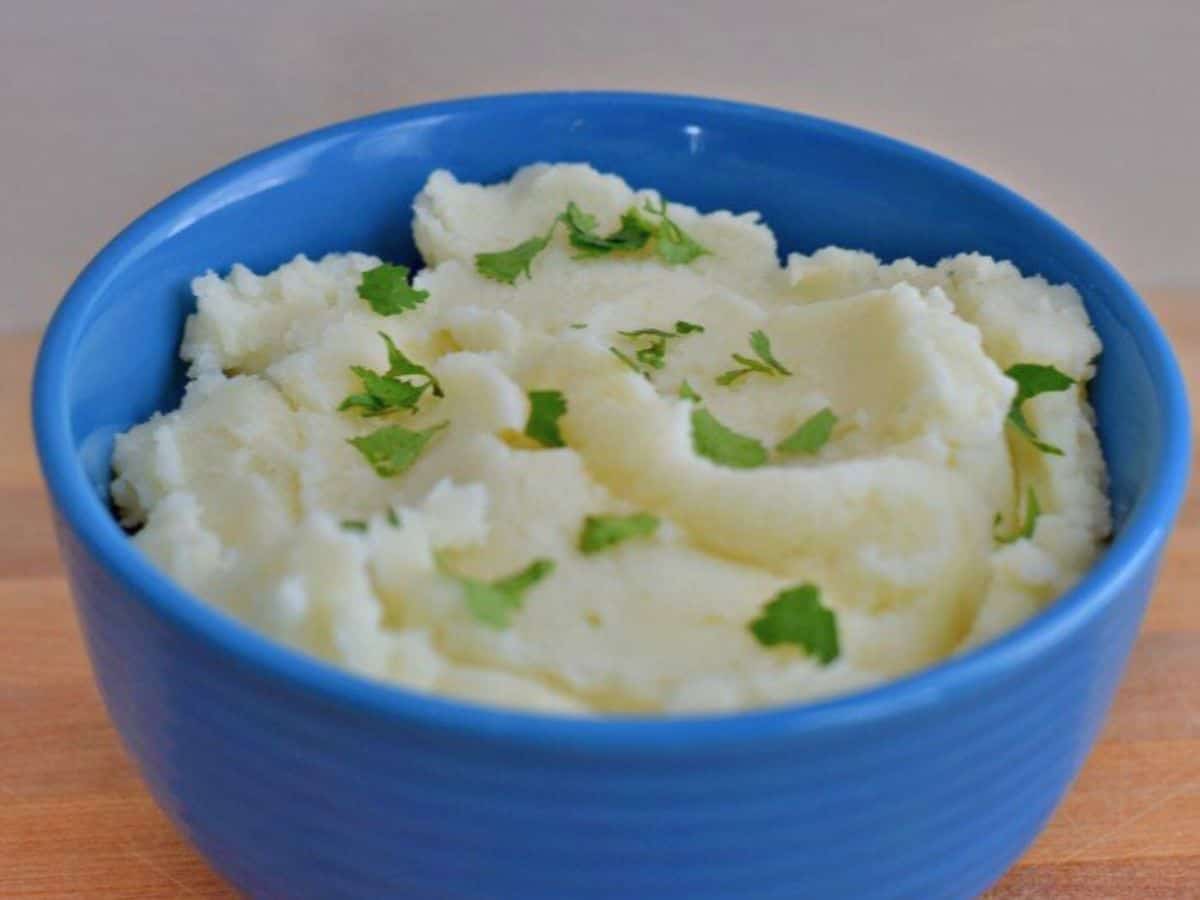 Overhead shot of a bowl of mashed potatoes in a blue bowl with parsley sprinkled over it.