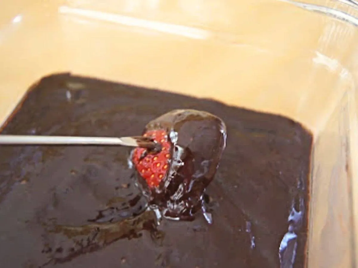 Image shows a fondue fork dipping a strawberry into chocolate fondue.