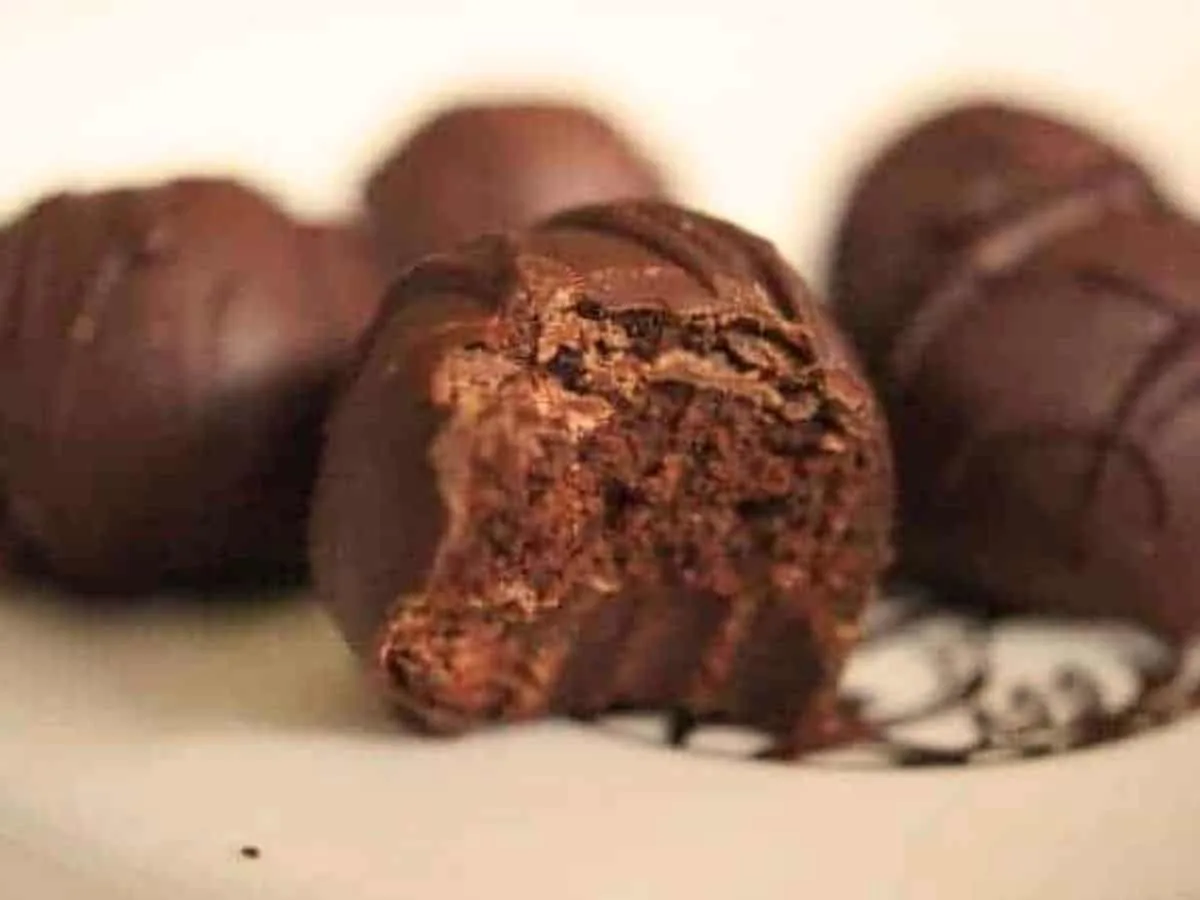 Image shows a brownie batter truffle on a plate with a bite taken from it and more behind it.