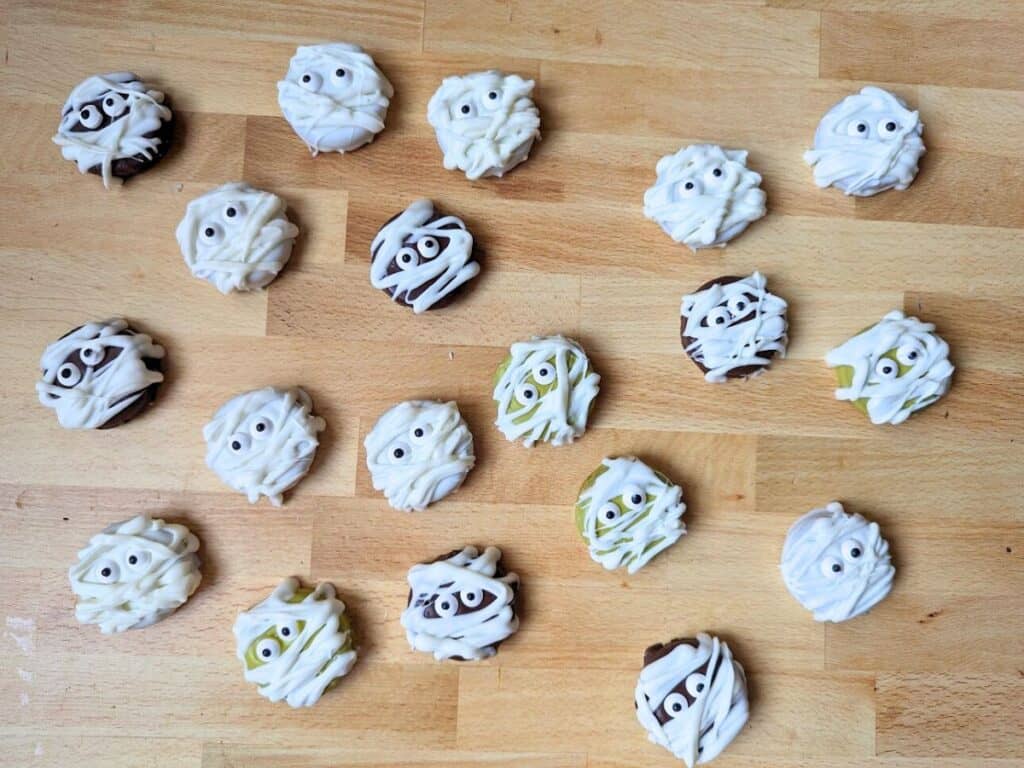 Image shows the Overhead of a whole bunch of Halloween mummy oreos on a wooden board.