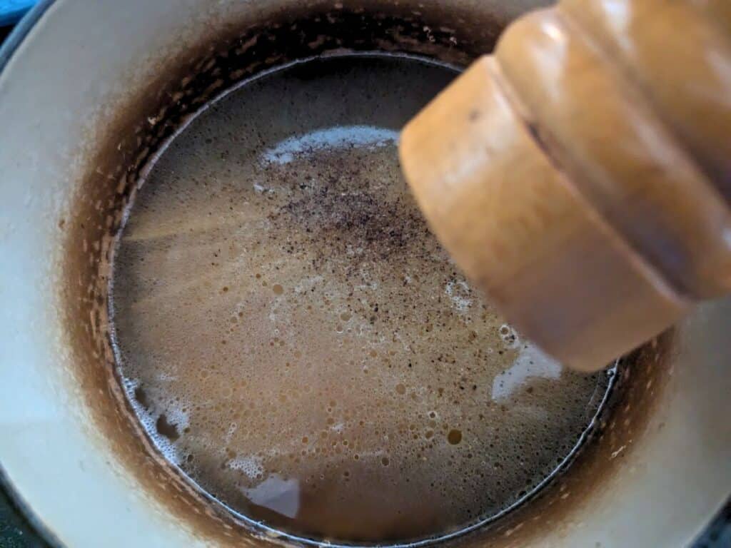 Image shows adding pepper into the pot with chicken stock.