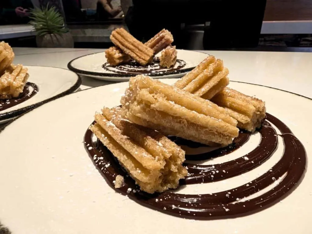 Image shows three plates with Churros with chocolate sauce on a bar.