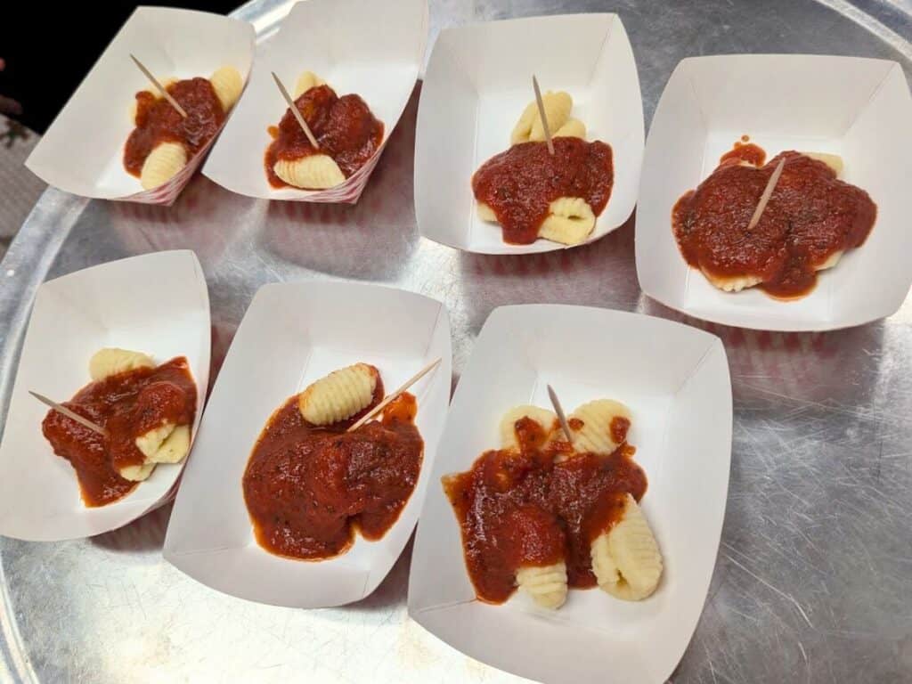 Image shows a tray with multiple containers holding gnocchi covered with tomato sauce.