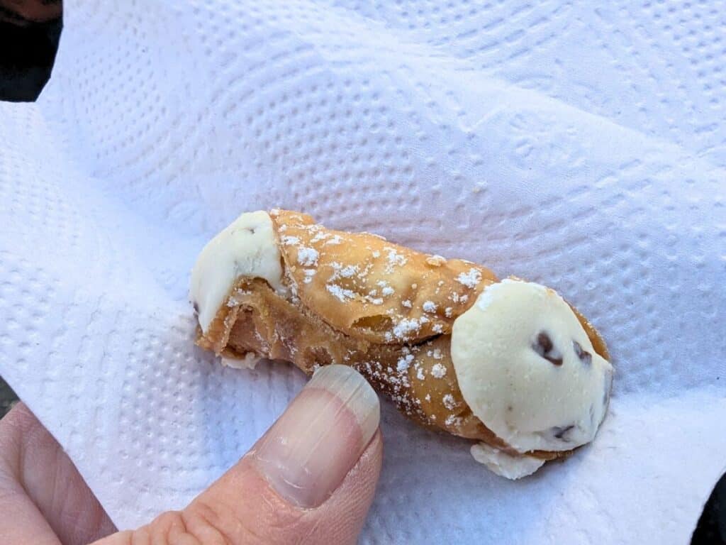 Image shows a hand holding a mini cannoli in a napkin.