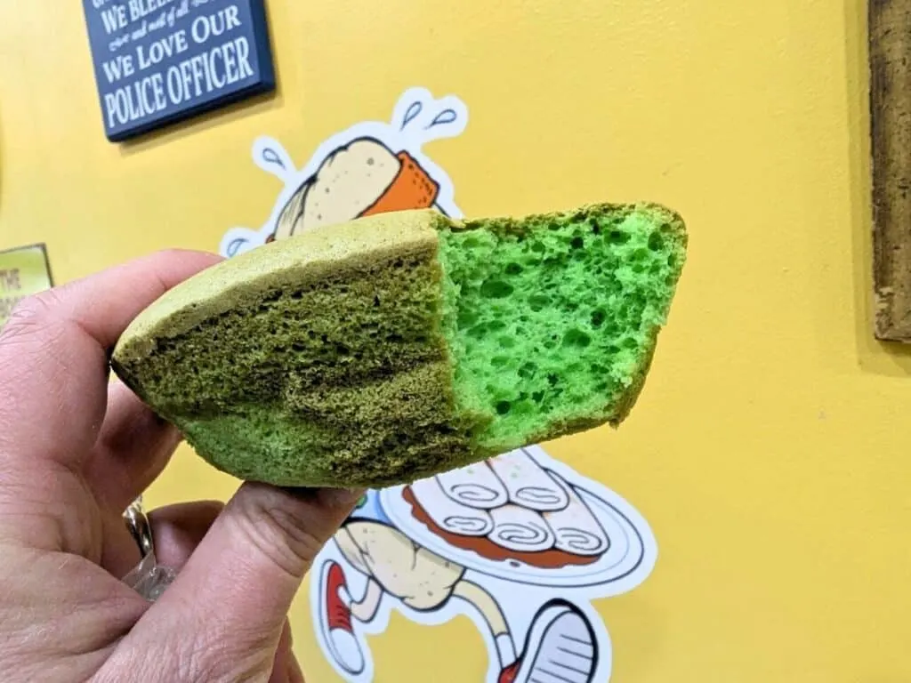 Image shows a hand holding a pandan sponge cake with a bite taken from it.