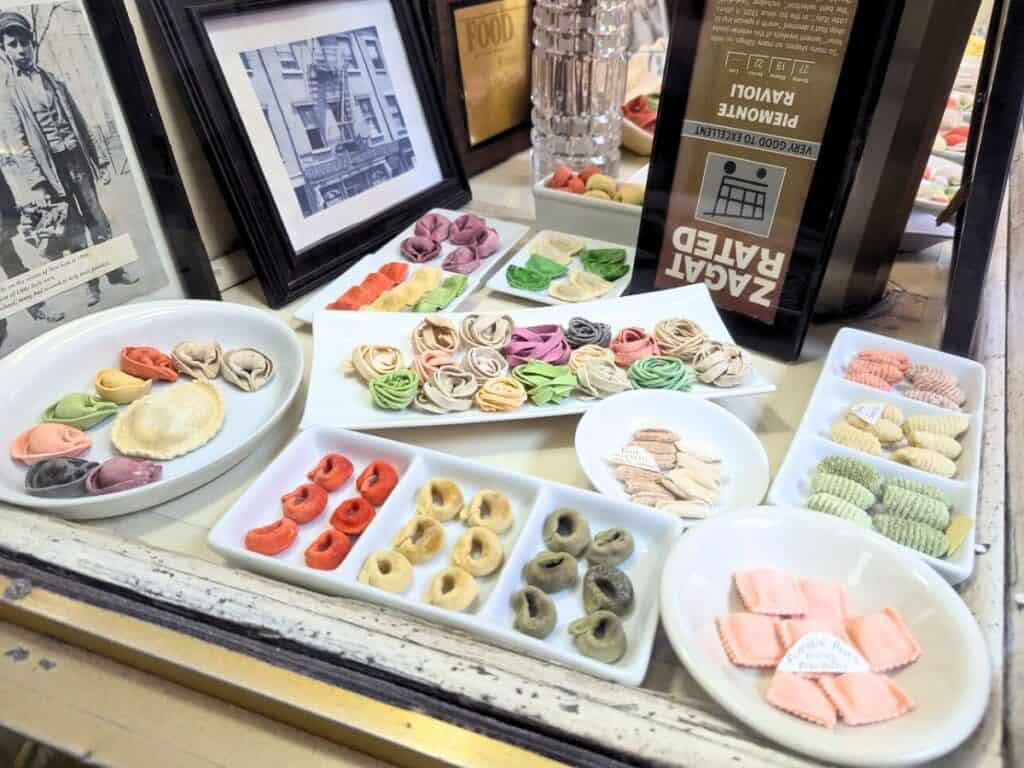 Image shows the front window of Piemonte Ravioli Company with different colorful pastas.