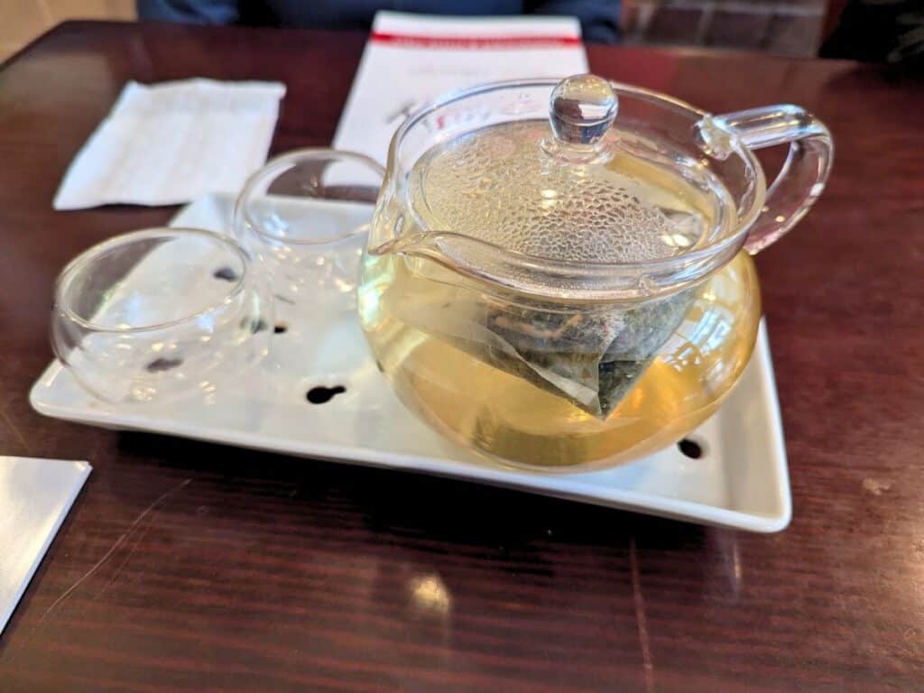 Image shows a glass Pot of Jasmine tea on a wooden table.