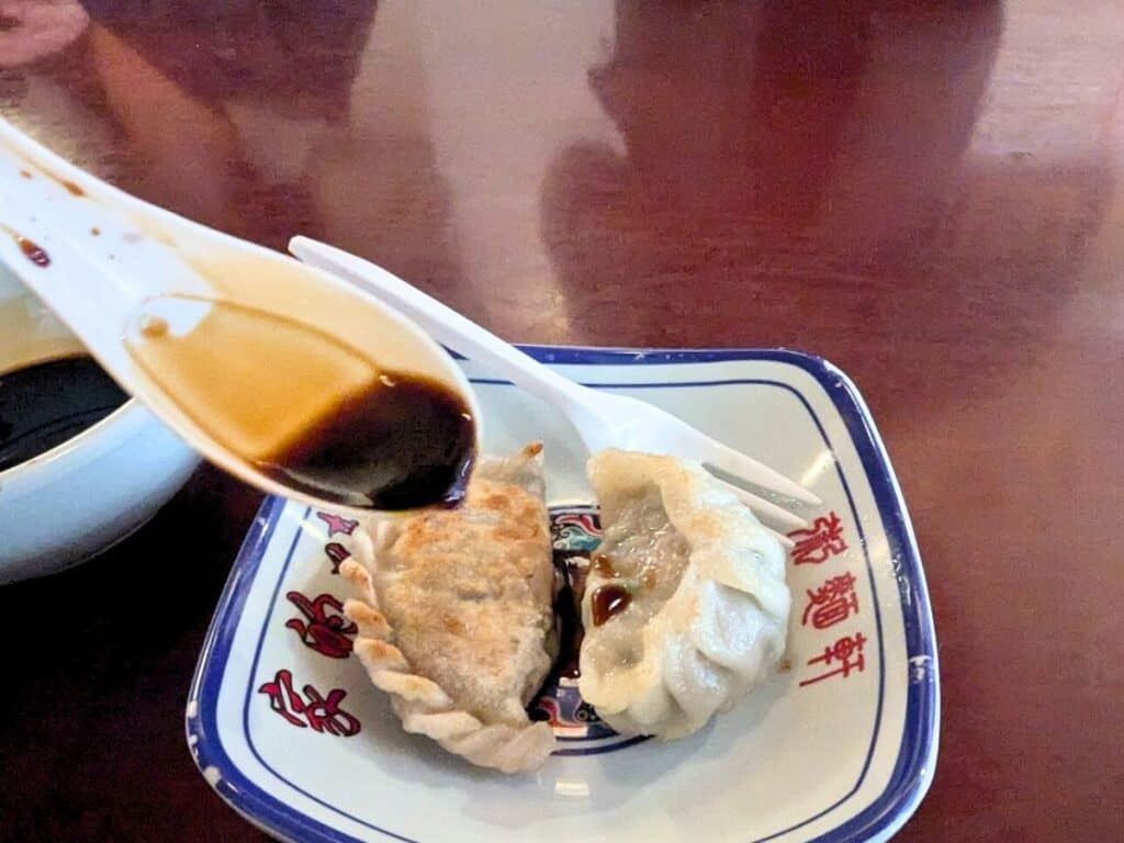 Image shows a spoon pouring sauce over two dumplings in a small bowl.