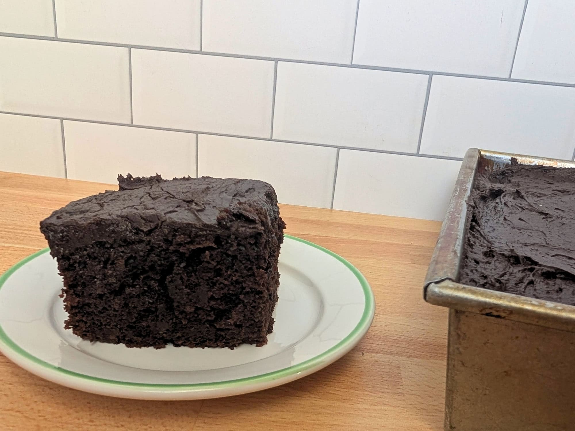 A slice of chocolate cake on a plate next to a 9x13 pan filled with the remaining cake.